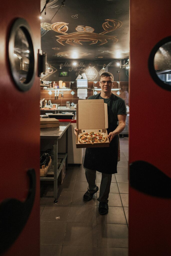 A chef presenting a delicious freshly baked pizza inside a cozy and modern restaurant kitchen.